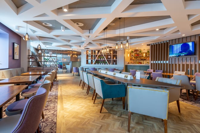 The Aspire Lounge at Edinburgh Airport features a seating area with tables and chairs, adjacent to a well-stocked bar.