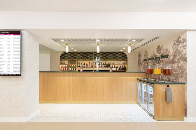 The bar at Edinburgh Airport's Escape Lounge offers a selection of spirits and beverages, with a flight information screen nearby.