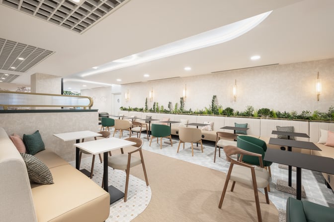 The seating area in Edinburgh Airport's Escape Lounge features tables and chairs with a backdrop of greenery for a relaxing atmosphere.
