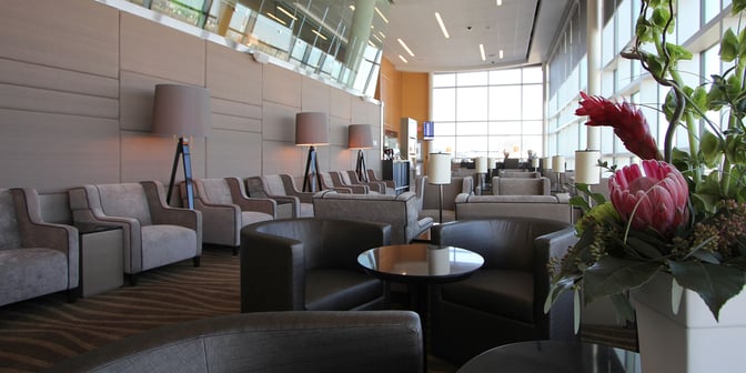 The seating area in the Plaza Premium Lounge at Edmonton International Airport features armchairs and tables with large windows providing natural light.