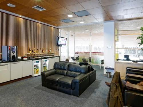 The lounge at El Tepual International Airport features a seating area with sofas and a self-serve beverage station with various drinks.