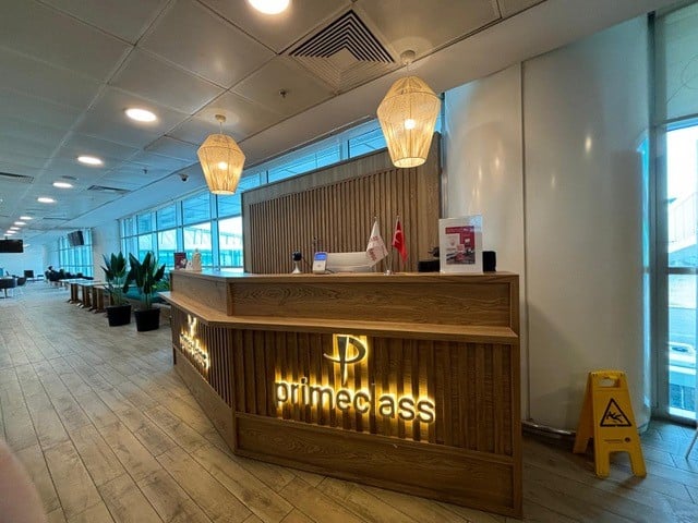 The Primeclass Lounge reception at Esenboğa International Airport features a wooden counter with signage, located near large windows and seating areas.