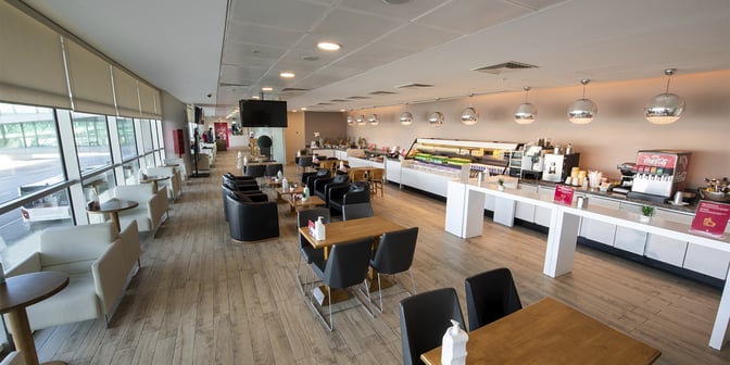 The Primeclass Lounge at Esenboğa International Airport features a self-serve food and beverage area with various seating options and airport views.