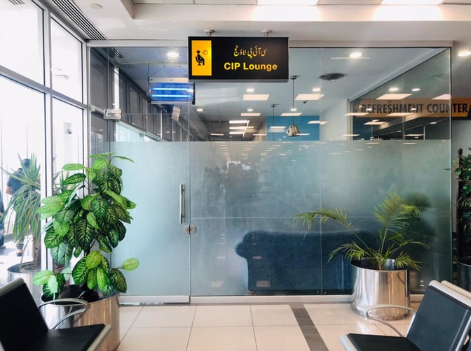 The entrance to the CIP Lounge at Faisalabad International Airport features glass doors and is located near a seating area.