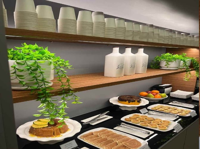 The food area at Blue Lounge in Fernando de Noronha Airport offers a selection of pastries, cakes, and fresh fruits.