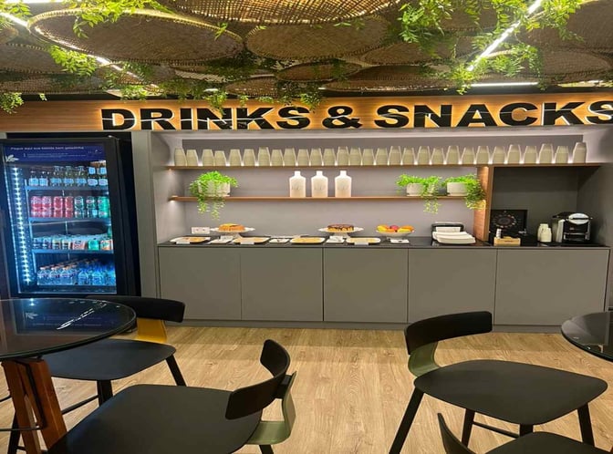 The drinks and snacks area at Fernando de Noronha Airport lounge features a self-serve beverage fridge and a selection of light refreshments.