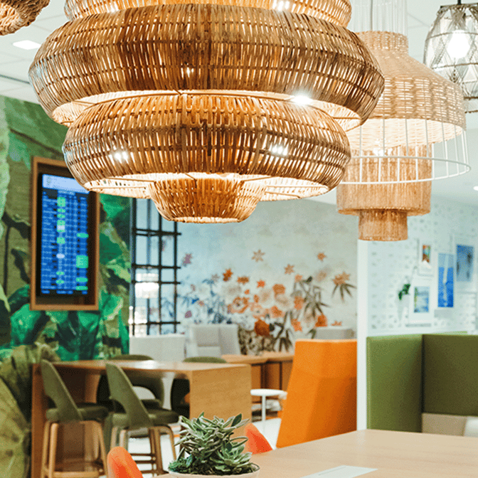 The seating area in Fort Lauderdale's Escape Lounge features tables, chairs, and a flight information display, with decorative wall art.