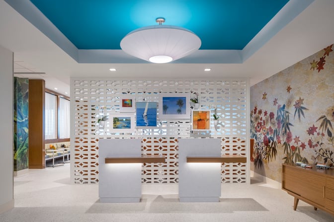 The reception area of the Escape Lounge at Fort Lauderdale Hollywood International Airport features check-in counters and decorative wall art.