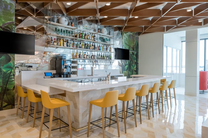The Escape Lounge at Fort Lauderdale Hollywood International Airport features a bar with counter seating and a selection of spirits and beverages.