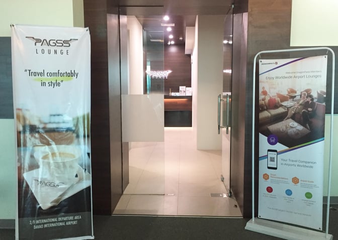 The entrance to the PAGSS Premium Lounge at Francisco Bangoy International Airport features promotional banners and a glass door entry.