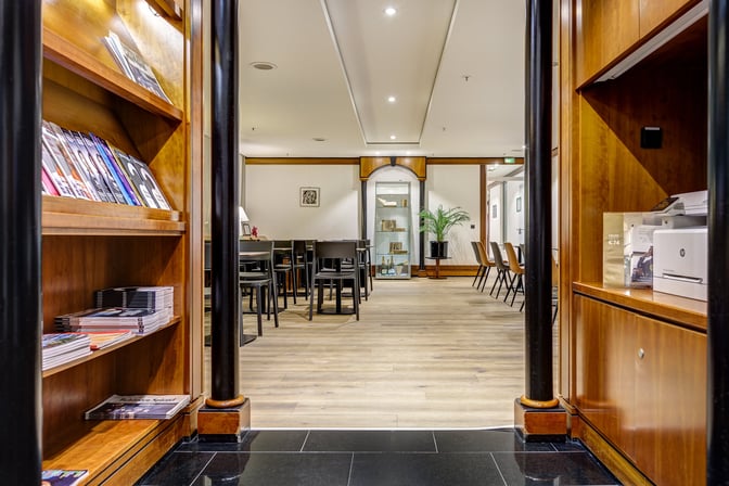 The LuxxLounge at Frankfurt Airport features a seating area with tables and chairs, adjacent to a magazine rack and printer station.