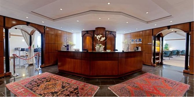 The LuxxLounge reception at Frankfurt Airport features a central desk with floral arrangements, flanked by seating and dining areas.