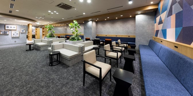 The seating area in the Lounge TIME/International at Fukuoka Airport features various chairs and sofas with small tables and plant decor.
