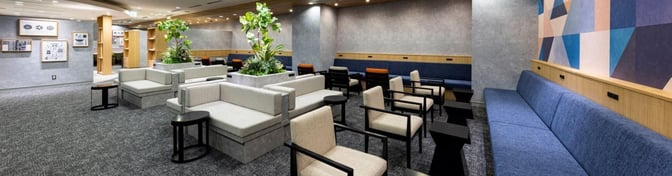 The lounge at Fukuoka Airport features varied seating options, including sofas and armchairs, with tables and decorative plants.