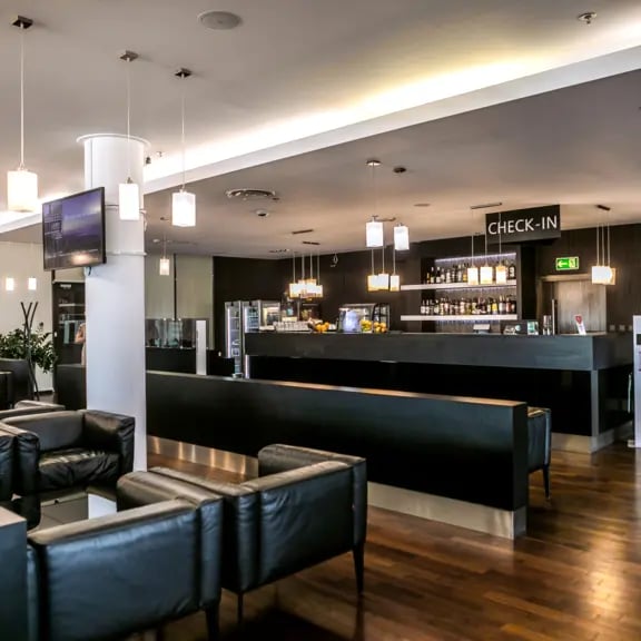 The Executive Lounge at Gdansk Lech Walesa Airport features a check-in counter and seating area with a bar offering beverages.