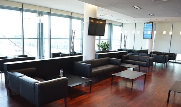 The Executive Lounge at Gdansk Lech Walesa Airport features comfortable seating with tables and a view of the airport through large windows.