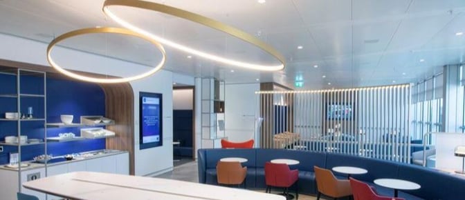 The Air France - KLM Lounge at Geneva International Airport features a seating area with tables and chairs, adjacent to a self-serve snack station.