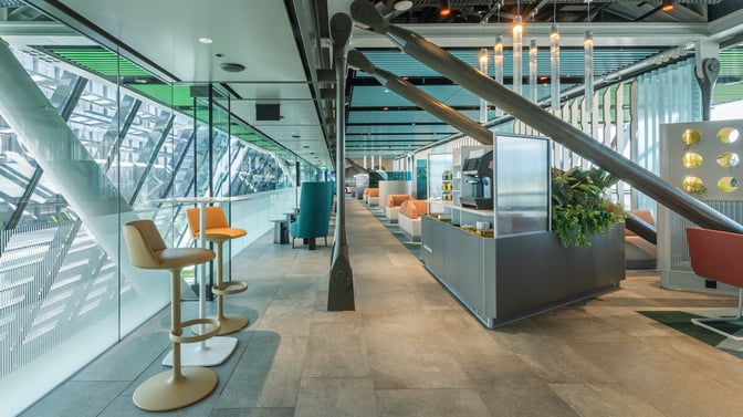 The Crystal Lounge at Geneva International Airport features high-top seating and a self-serve beverage station, with views of the tarmac.