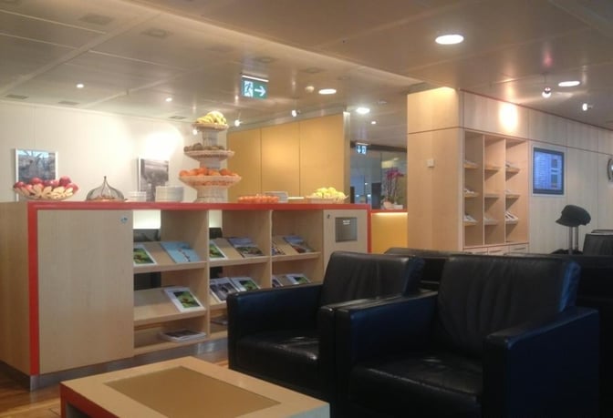 The Swissport Horizon Lounge at Geneva International Airport features a seating area with armchairs and a self-serve fruit station.