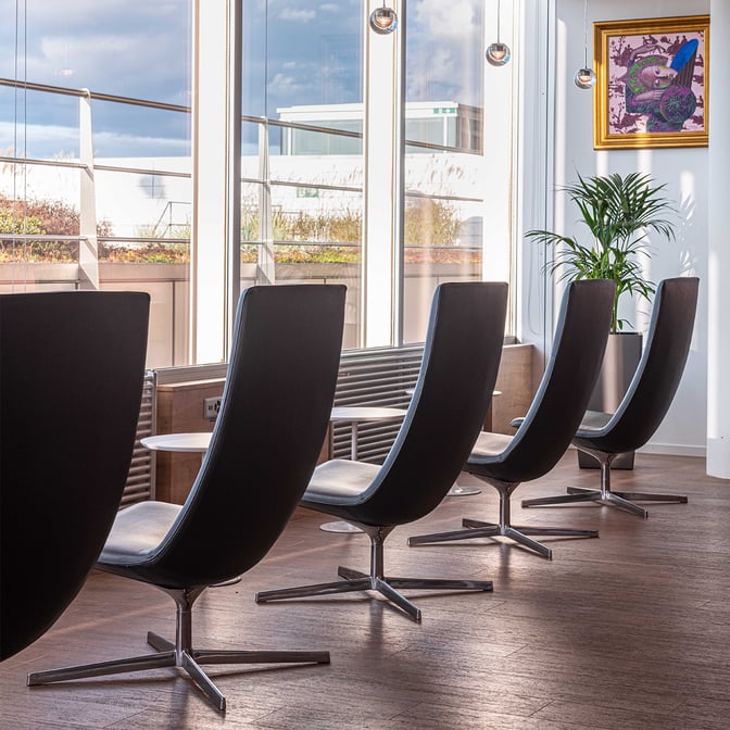 High-backed swivel chairs in the marhaba Lounge at Geneva International Airport offer seating with views of the tarmac through large windows.