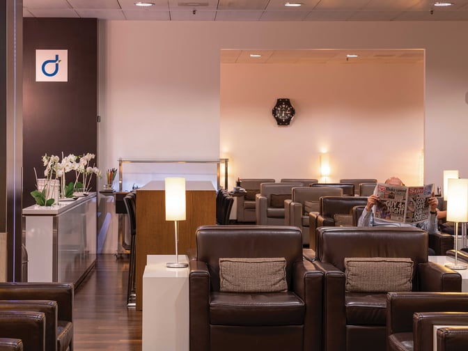 The Marhaba Lounge at Geneva International Airport features comfortable seating with individual lamps and a reading area for travelers.
