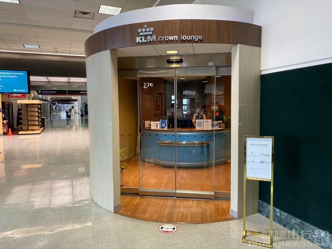 The KLM Crown Lounge entrance at George Bush Intercontinental Airport features a curved glass door and a welcome sign listing partner airlines.