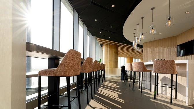 The Club GRR at Grand Rapids Airport features a bar area with high seating and large windows offering runway views.