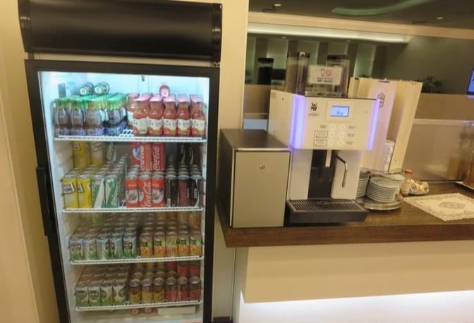 The Korean Air Lounge at Gimhae International Airport features a beverage station with a stocked fridge and a self-serve coffee machine.