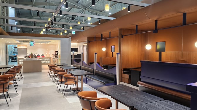 The N Sky Hub Lounge at Gimhae International Airport features a dining area with tables and chairs, adjacent to a self-serve food station.