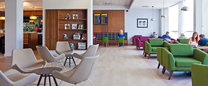 The UpperDeck Lounge at Glasgow Airport features a seating area with armchairs, a bar, and a magazine rack for travelers.