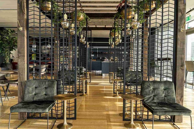 Seating area in The Lounge by Menzies Aviation at Gothenburg Landvetter Airport features individual chairs with small side tables and decorative partitions.