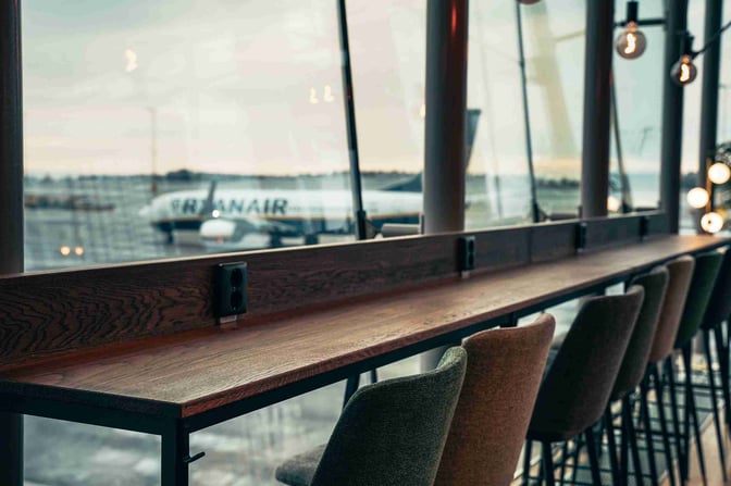 High stools and a counter with power outlets in The Lounge by Menzies Aviation offer airport views at Gothenburg Landvetter.