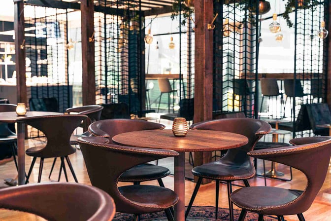 The seating area in The Lounge by Menzies Aviation at Gothenburg Landvetter Airport features round tables and chairs for dining.