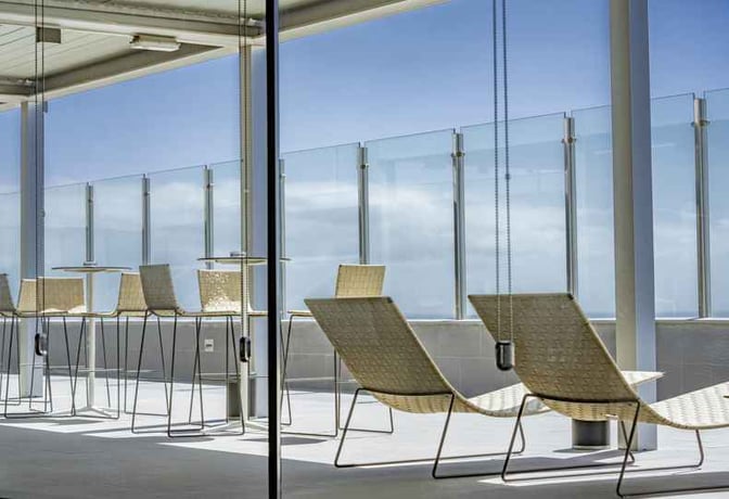 The outdoor seating area at Sala Galdós in Gran Canaria Airport features wicker chairs and high tables with glass paneling.
