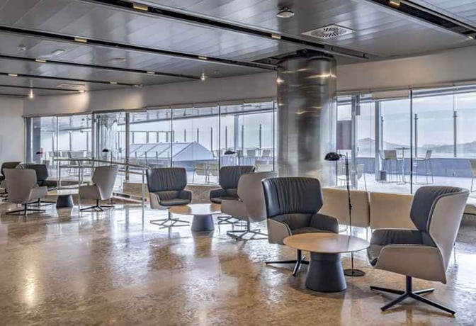 The seating area in Sala Galdós at Gran Canaria Airport features comfortable chairs and tables with views of the tarmac.