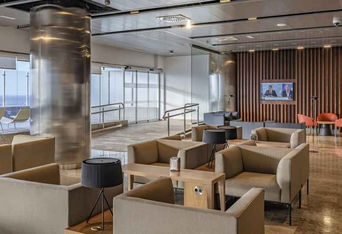 The seating area in Sala Galdós at Gran Canaria Airport features comfortable chairs, tables, and a television for passenger relaxation.