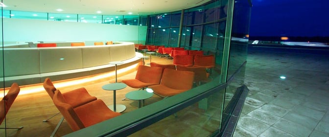 The VIP Lounge at Graz Airport features spacious seating with tables, offering views of the tarmac through large windows.