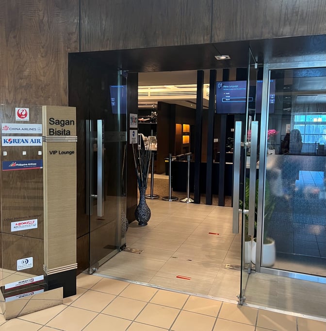 The entrance to the Sagan Bisita VIP Lounge at Guam International Airport features glass doors and signage for various airlines.