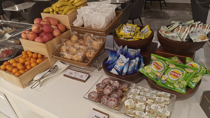 The snack station at China Southern First/Business Class Lounge in Guangzhou offers a variety of fruits, packaged snacks, and pastries.