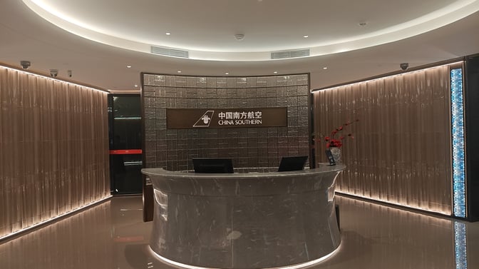 The reception area of the China Southern First/Business Class Lounge at Guangzhou Baiyun International Airport features a curved desk and signage.