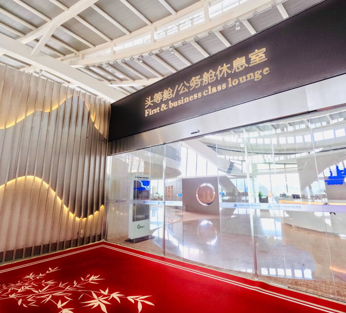 The entrance to the First and Business Class Lounge at Guilin Liangjiang International Airport features glass doors and a welcoming sign.