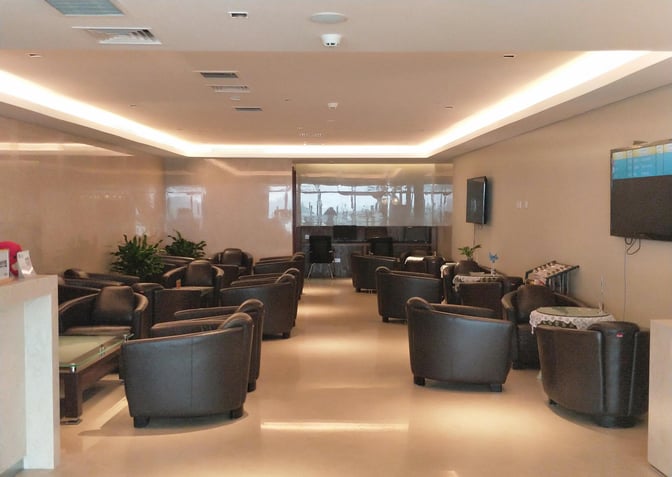 The seating area in Guilin Liangjiang International Airport's lounge features comfortable chairs and tables, with a TV and a workstation in the background.