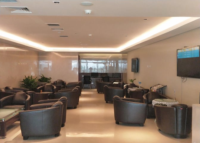 The seating area in the First Class/Business Class Lounge at Guilin Liangjiang International Airport features armchairs and tables with a view of flight information screens.