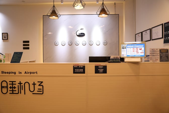 The reception desk at Haikou Meilan International Airport's Sleeping in Airport Hotel provides check-in services with informational signage and a digital display.