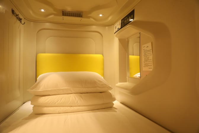A sleeping pod at Haikou Meilan International Airport features a bed with pillows and a small shelf with a mirror.