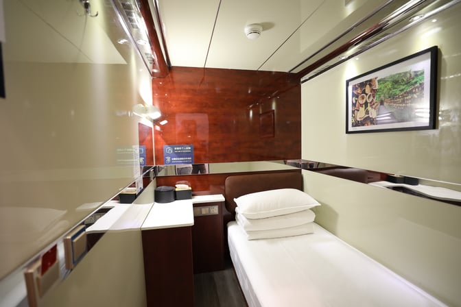 A compact sleeping pod at Haikou Meilan International Airport features a single bed, bedside table, and wall-mounted artwork.
