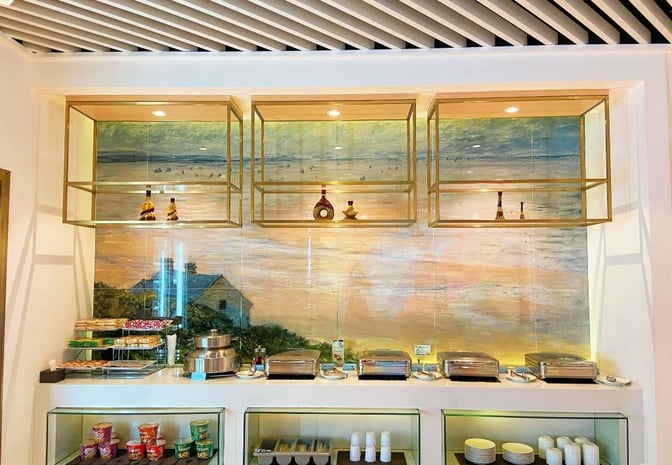 Self-serve food area at Trvok Lounge, Haikou Meilan International Airport, offers hot dishes, snacks, and beverages with decorative shelving.