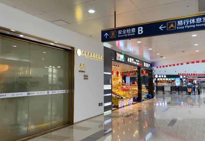 The entrance to the Trvok Lounge at Haikou Meilan International Airport is located near a security check and retail stores.