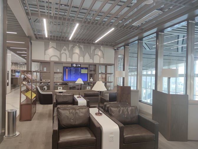 Seating area in Hainan Airlines Lounge at Haikou Meilan International Airport features armchairs, a flight information screen, and reading materials.