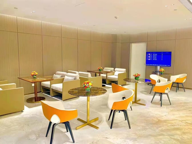 The seating area in Business Lounge 4 at Haikou Meilan International Airport features tables, chairs, and a flight information screen.